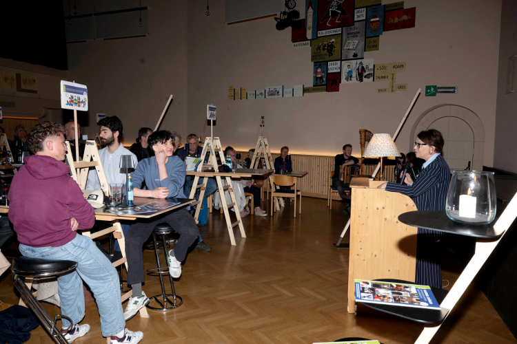 Gerti Verdorfer (am Pult) hält die Lobrede auf die Sieger des Gabriel-Grüner-Preises: Luis Parth, am Tisch (rechts), neben ihm Dolev Nahoom, der Musiker, den Parth und Noah Frischmann begleitet haben.