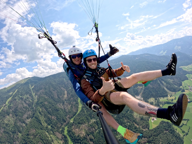Unser Redaktionsnachwuchs auf Recherche und der Suche nach dem Abenteuer: Im Bild fliegt Max Hofer (mit dem blauen Helm) bei einem Tandemflug vom Kronplatz herunter.